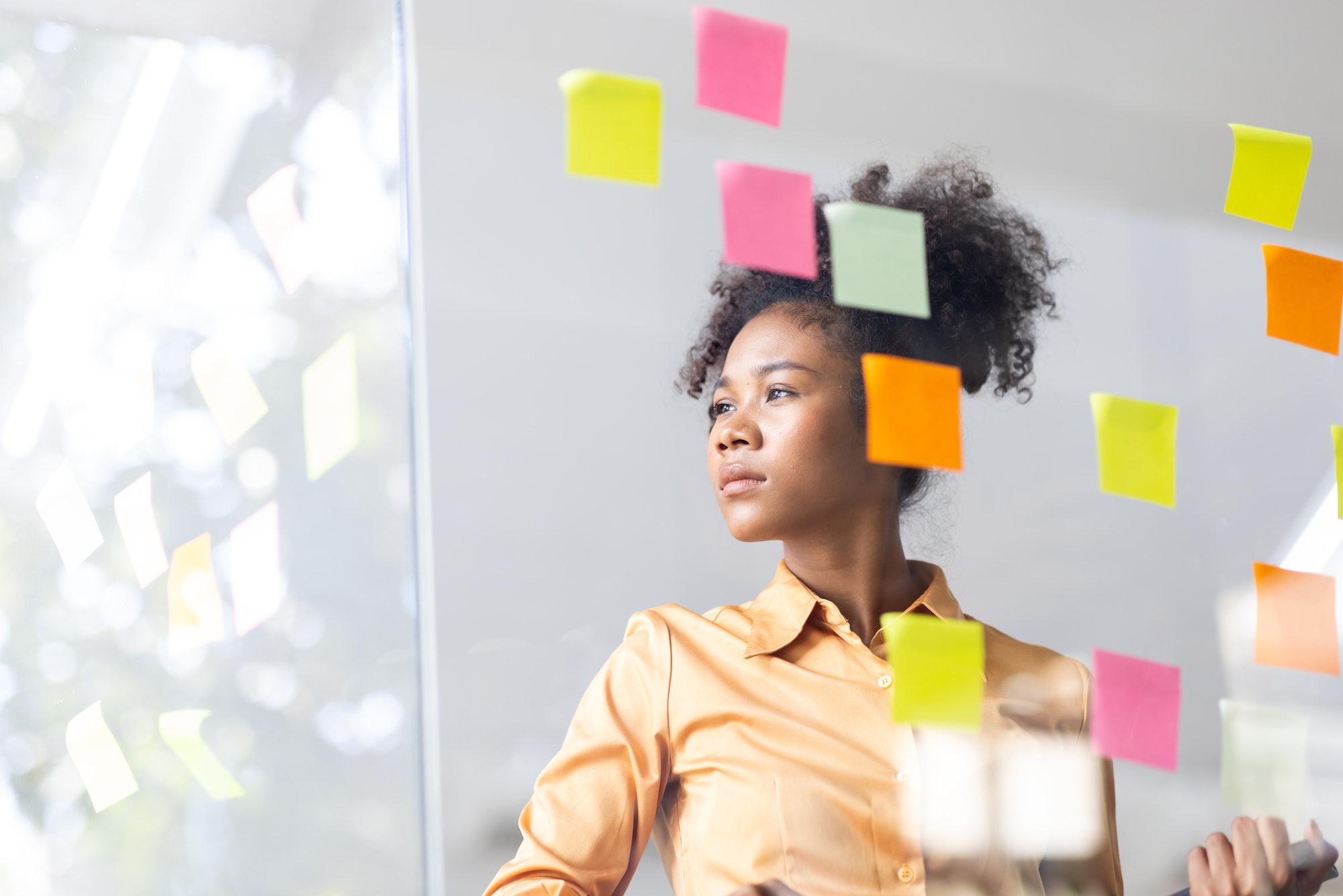 Business female employee with many conflicting priorities arranging sticky notes commenting and